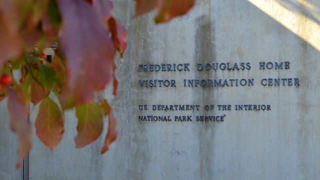 A sign for the Frederick Douglass National Historic Site visitor center with leaves in foreground