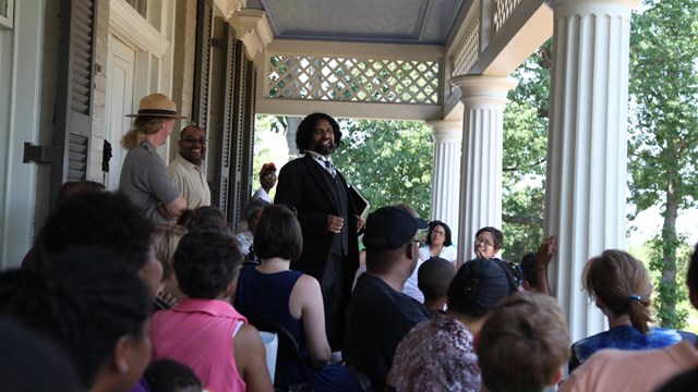 An actor dressed as Frederick Douglass talks to a crowd