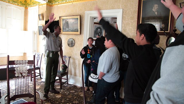 A ranger talks with a group of students in a historic parlor