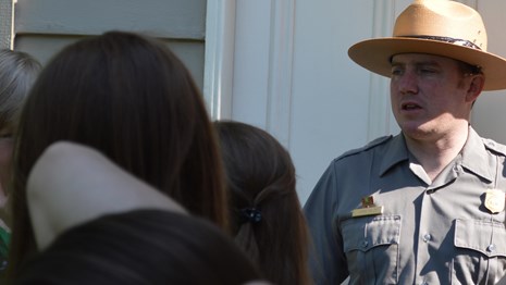 A group of students interacts with a ranger outside a historic house