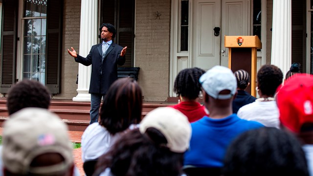 A man dressed as Frederick Douglass speaks to a crowd