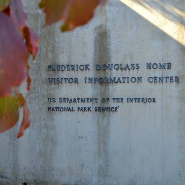 A sign for the Frederick Douglass National Historic Site visitor center with leaves in foreground