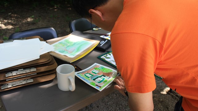 Man leaning over table to paint watercolor image.