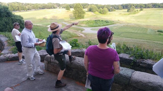 Uniformed park ranger points to a field with people looking on