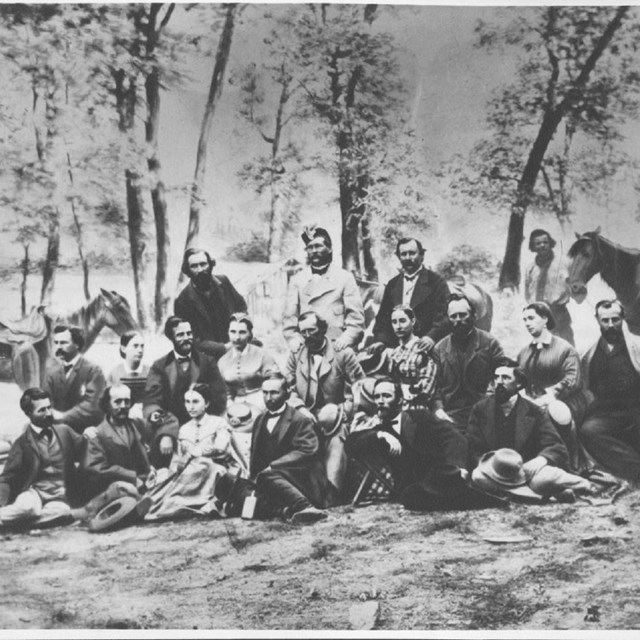 black and white of group of people sitting on forest floor with trees around posing 