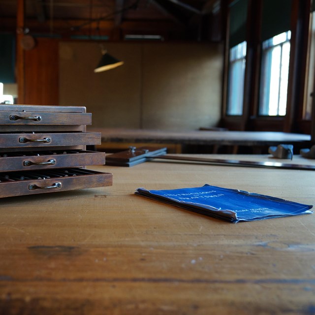 Wooden box with four small shelves and blue book sit on top of wooden table.