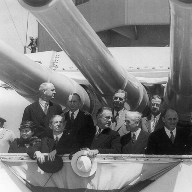 Frances Perkins sits with a delegation under the turrets of a battleship.