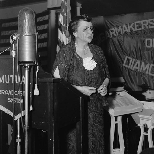 Frances Perkins stands behind a podium and microphone