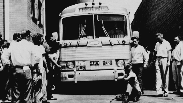 A white man sits in front of the Freedom Riders' bus, trying to prevent it from leaving the station