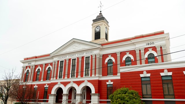 A brick and stone building with a clocktower. Calhoun County Courthouse is written on the side.