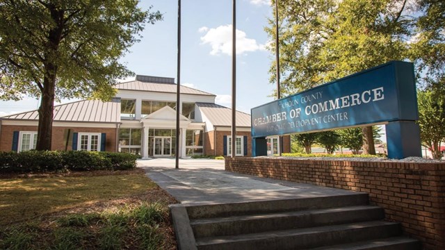 A brick and metal two story building. A Chamber of Commerce sign and flagpoles are in front. 