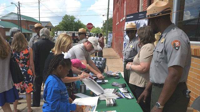Several people with ranger hats stand behind a table with greeting people visiting the table.