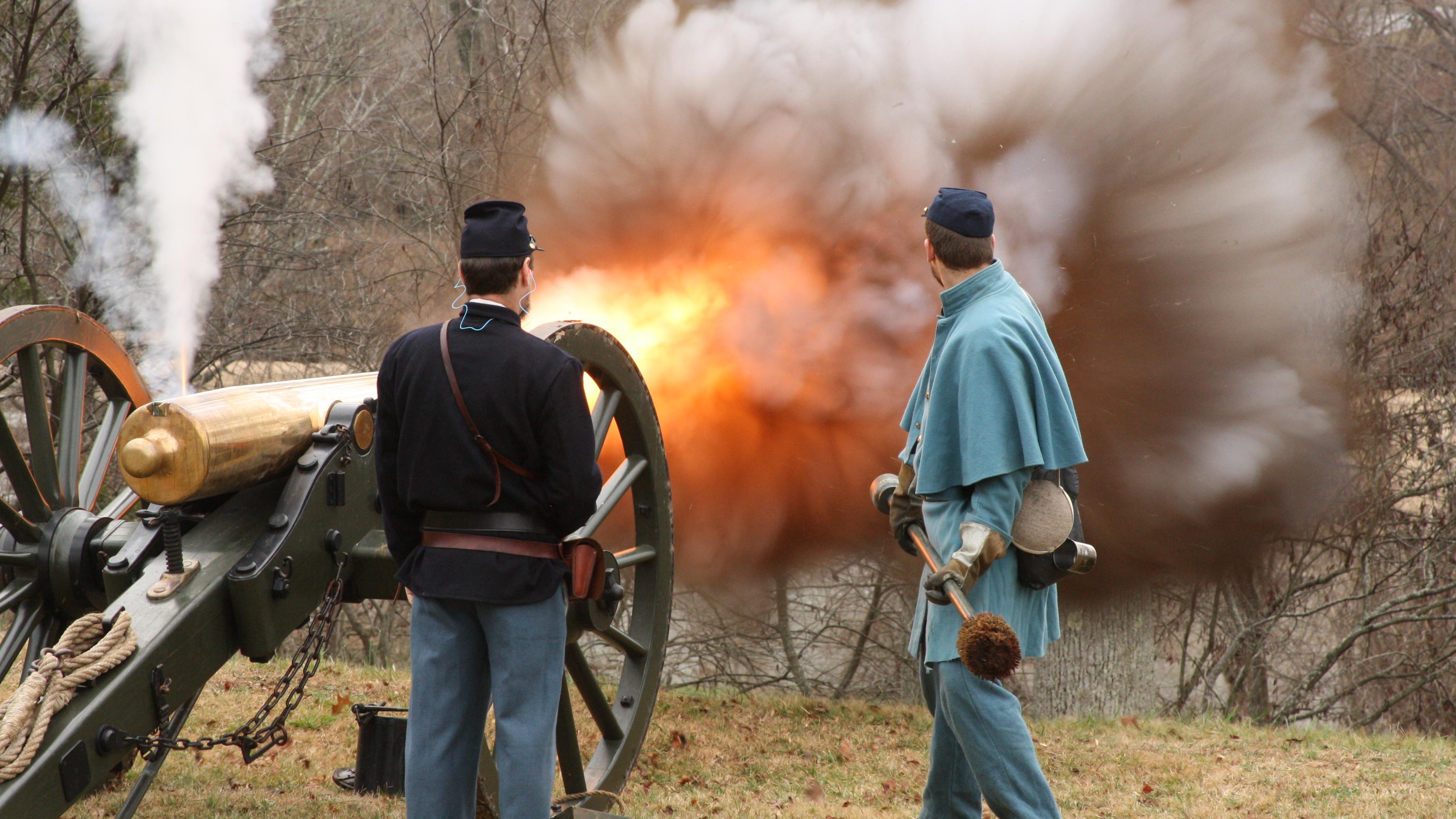 Two living historians stand aside cannon as it fires