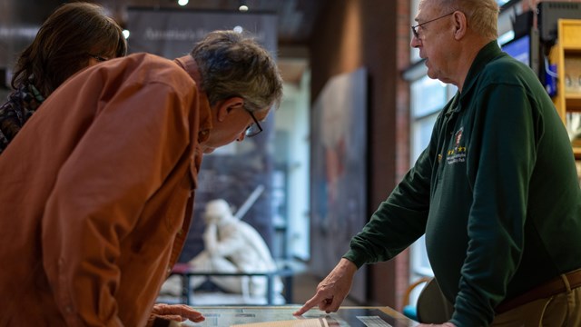 A park volunteer speaking with two people at a visitor center desk.