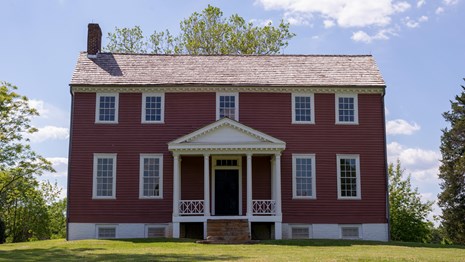 A two story red manor house with entrance columns.