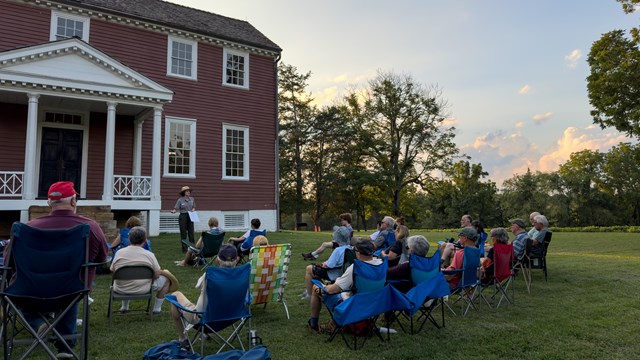 A ranger speaks to people on a lawn outside a historic house.