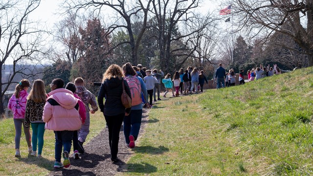 A large group of children and adults walk on a trail 