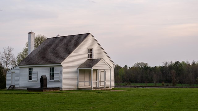 A one and a half story white house in a mowed field.