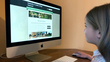 A color photograph of a 9 year old girl looking at a computer screen.