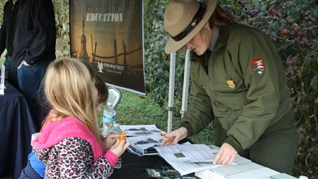 A ranger works with two young visitors on their Junior Ranger programs.