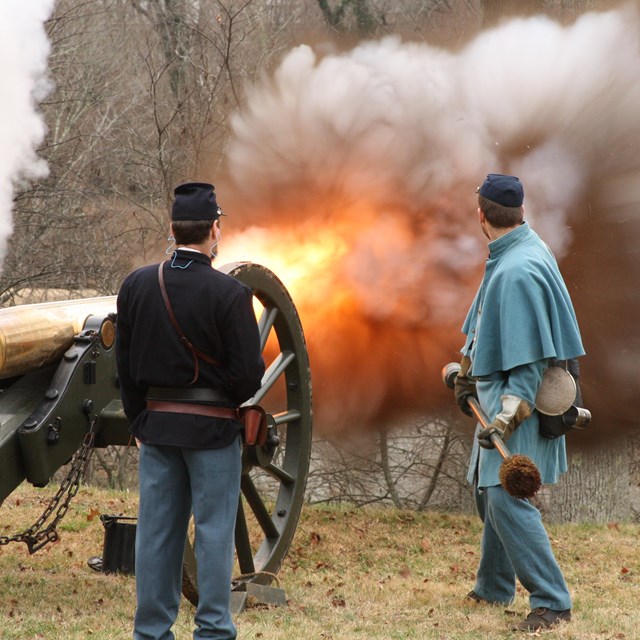 Two living historians stand aside cannon as it fires