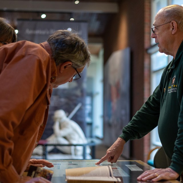 A park volunteer speaking with two people at a visitor center desk.