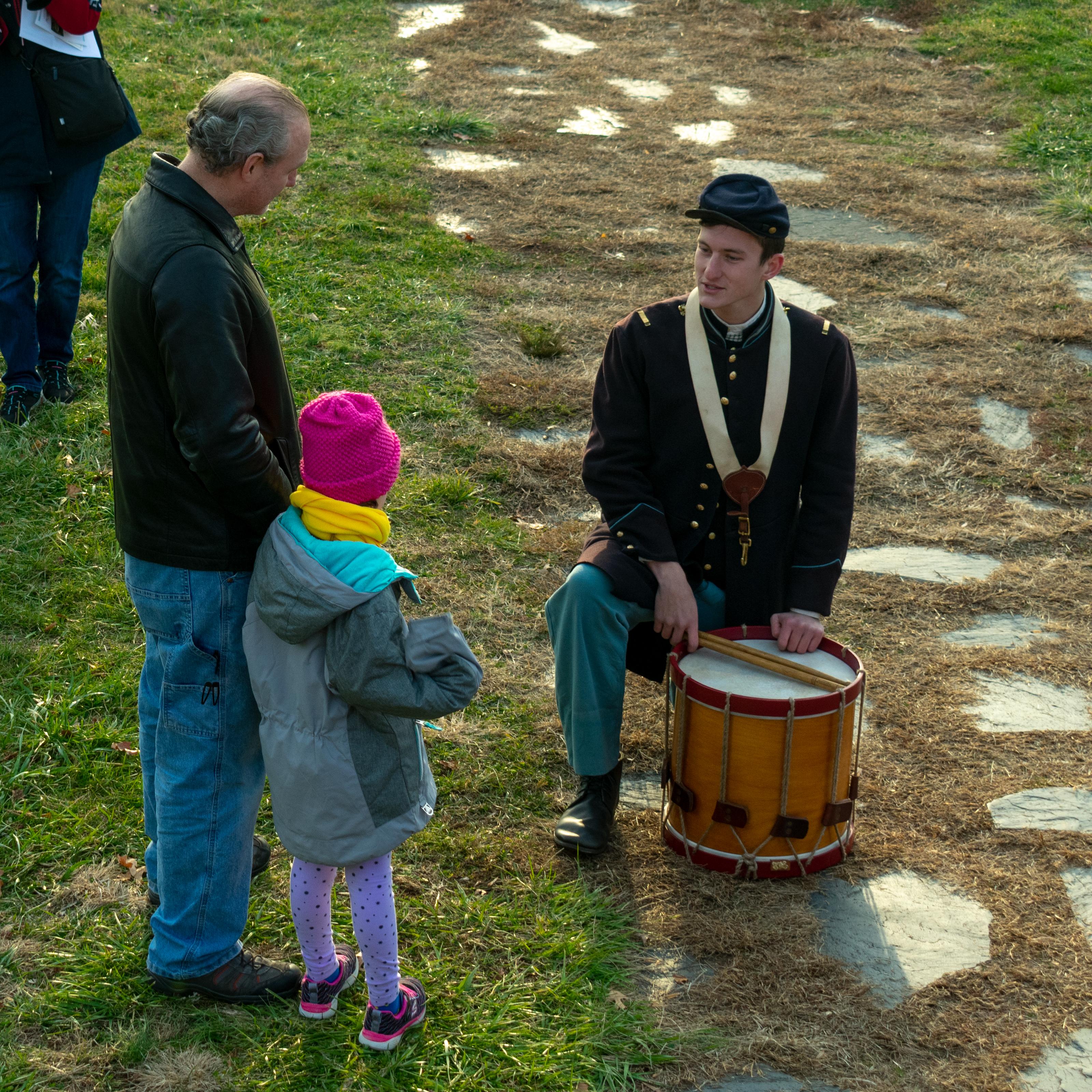 A man in blue Union uniform and drum speaking with three children.