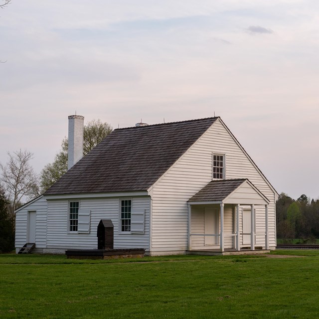 A one and a half story white house in a mowed field.