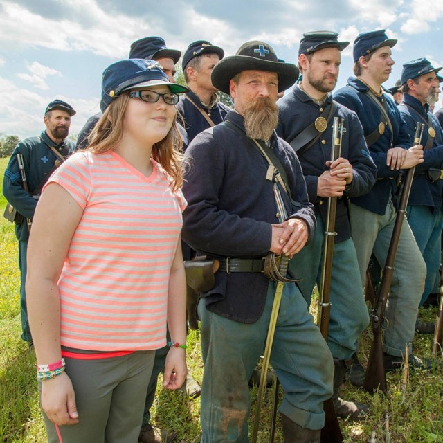 A young girl wearing a Civil War hat stands in line with federal reenactors 