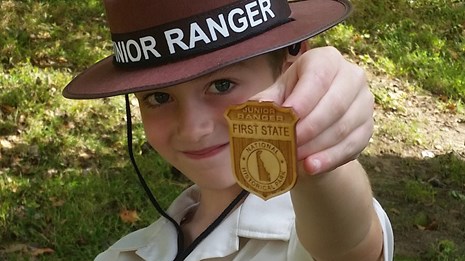A young boy holds up a wooden First State Junior Ranger Badge