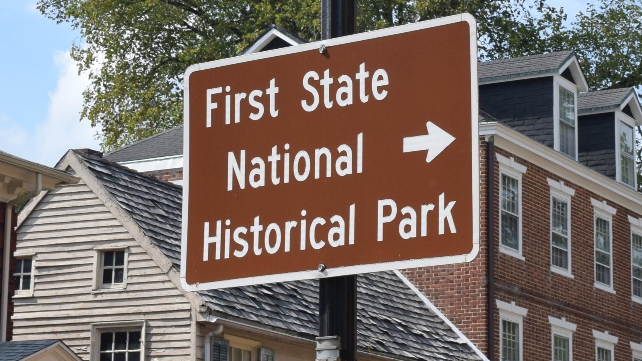 A brown sign on a black lightpole with the words "First State National Historical Park"