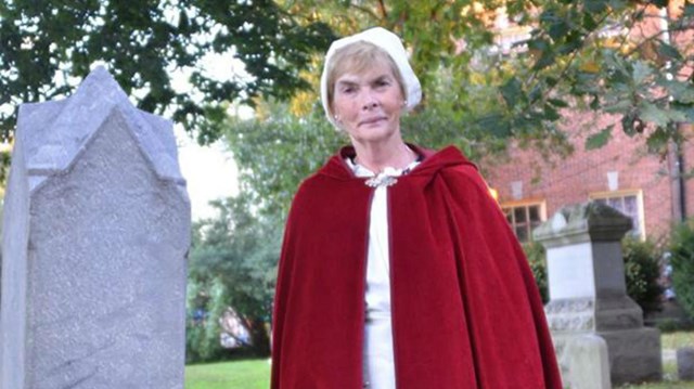 A women wearing a red cloak stands next to a grave at Old Swedes Church. 