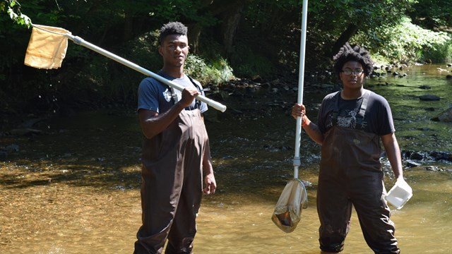 Two men stand in the creek while searching for macroinvertebrates. 