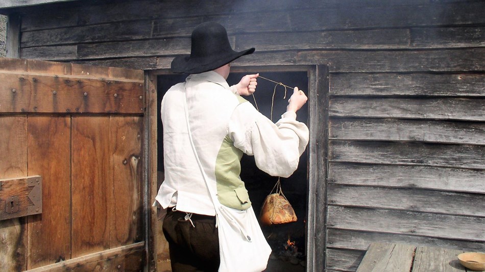 A gentleman is hanging meet in the smokehouse at the John Dickinson Plantation.