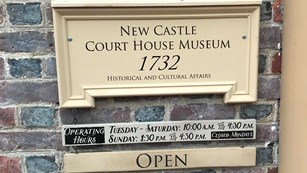 A sign hangs on the wall that says "New Castle Court House Museum" with the operating hours listed. 