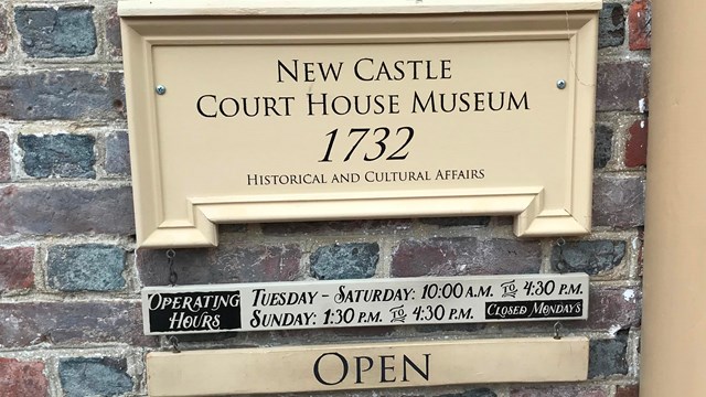 A sign hangs on the wall that says "New Castle Court House Museum" with the operating hours listed. 