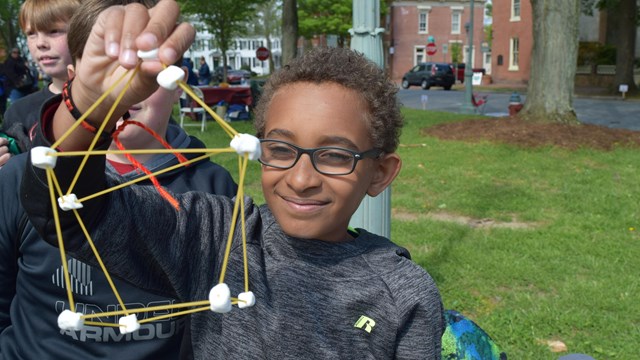 A young boy makes a structure using spaghetti and marshmallows. 