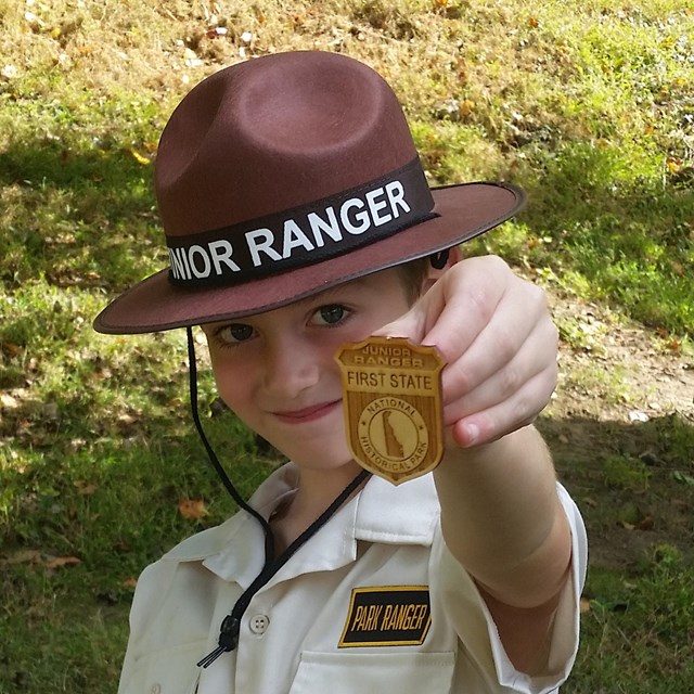 A young boy holds up a wooden First State Junior Ranger Badge