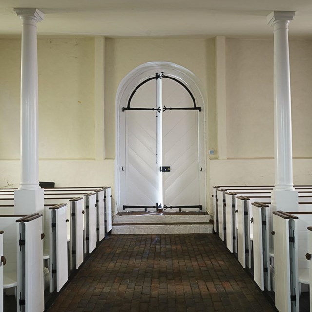 Light shines through a church door that is cracked open. 