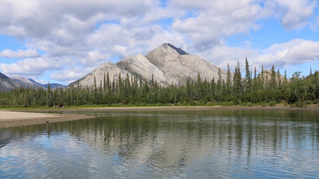 Distant mountain reflecting off John River with clouds in sky