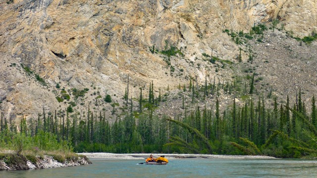 A person packrafting on the Alatna River below a mountain cliff