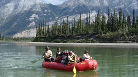 A raft with four paddlers on the Alatna River with the Brooks Range in the background