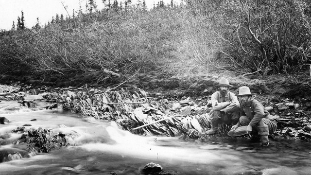 Historic photo of two miners alongside a gold-bearing creek in the Brooks Range