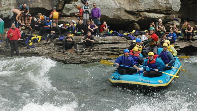 spectators watch as a raft plunges into the rapids