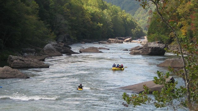 two kayaks and a raft on a boulder-strewn river