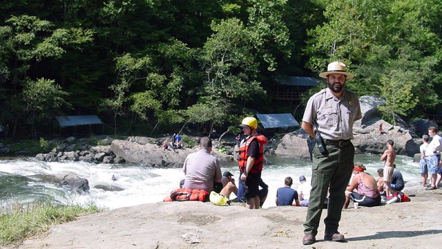 park ranger standing in front of river and rafters
