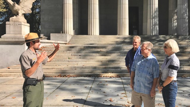 A ranger giving a program in front of the light granite columns, steps and eagle statue of the tomb