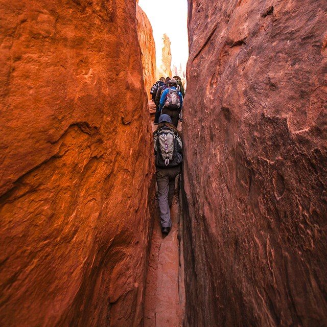 people hiking through narrow opening in red rock formation