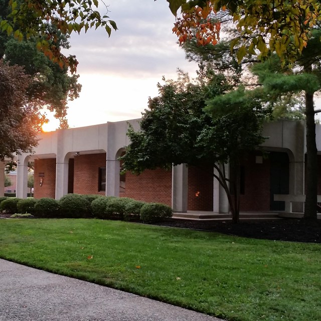a small, square, brick and concrete, brutalist style building surrounded by trees and grass.  