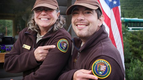 Two volunteers pointing to the patches on their jackets 